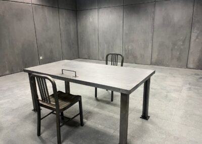 Mesa metálica y dos sillas en una sala con paredes de imitación de hormigón