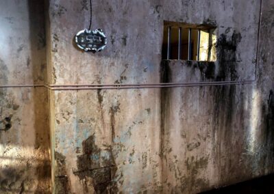 Muro envejecido con manchas de humedad, una tubería y un ventanuco con barrotes