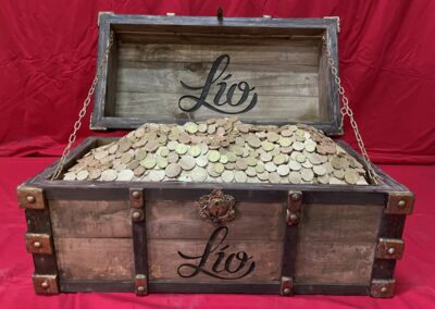 Cofre de madera envejecida con herrajes, abierto y lleno de monedas, con el logotipo de Lío