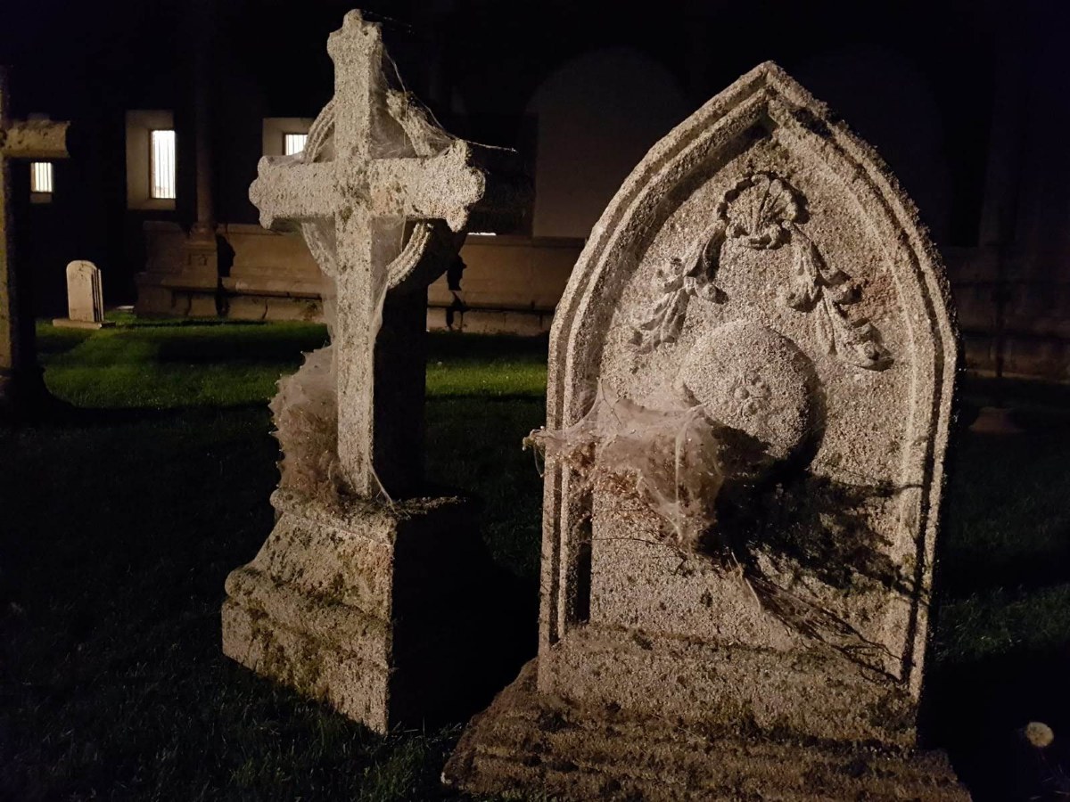Cruz de piedra y lápida ojival en un cementerio de noche