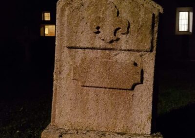 Lápida de piedra envejecida con una flor de lis, de noche