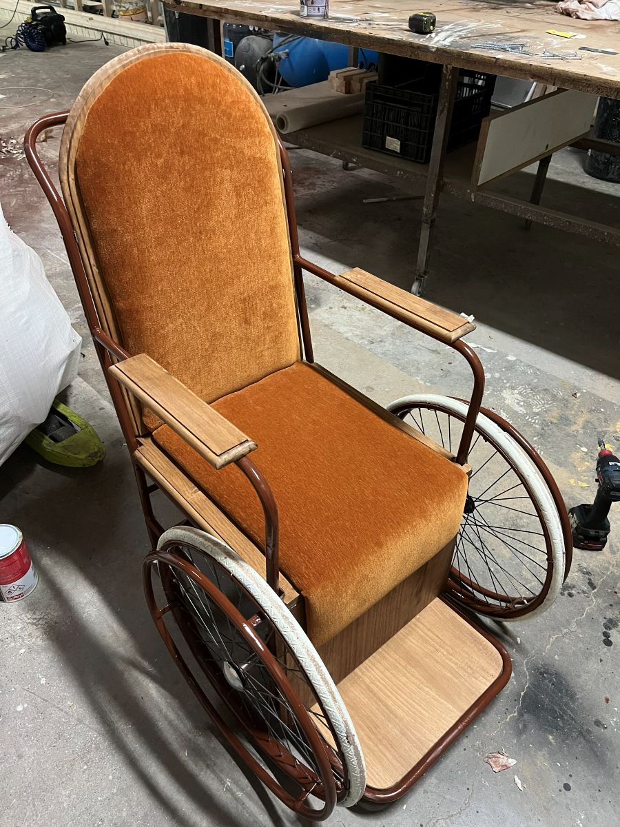 Silla de ruedas de época con asiento de terciopelo naranja y ruedas de madera