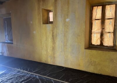 Estancia de la cabaña en construcción, con paredes amarillas envejecidas y ventanas de madera