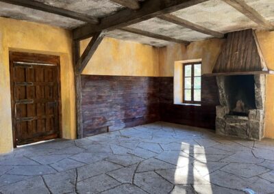Estancia de la cabaña con suelo de losas, chimenea de piedra y puerta de madera