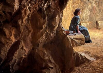 Actriz sentada sobre una roca dentro de la cueva construida en plató