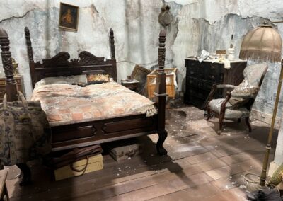Habitación secreta con cama de columnas, cómoda y butaca, cubierta de polvo