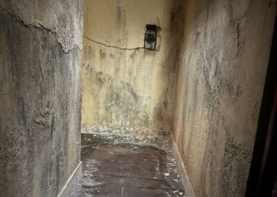 Pasillo de muros desconchados con un farol de pared al fondo