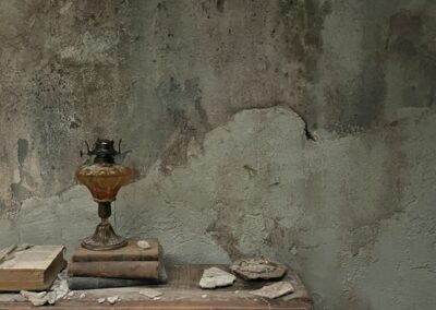 Quinqué y libros viejos sobre una repisa ante un muro desconchado