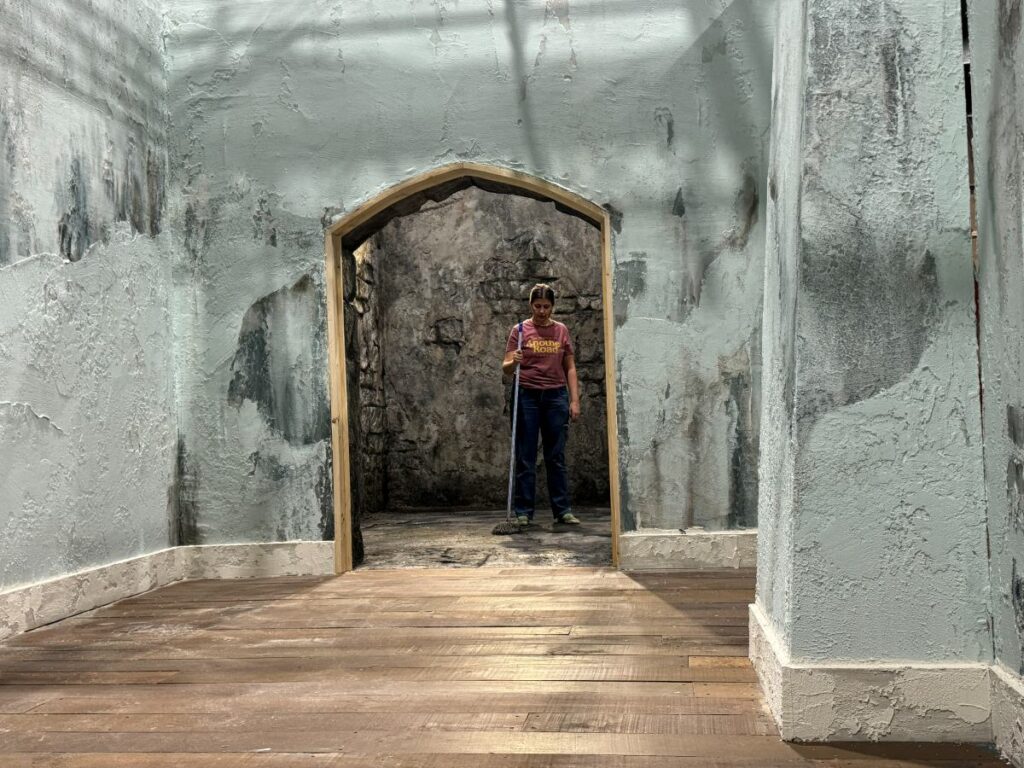 Pasillo de muros de piedra desconchados con un arco al fondo, construido en plató