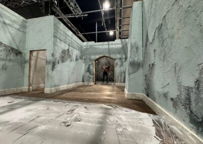 Pasillo de muros desconchados en tonos verdosos con un arco al fondo, en plató