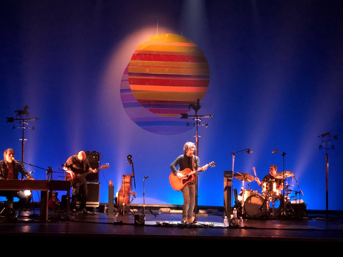 Quique González en concierto con un gran sol de franjas de colores suspendido sobre el escenario