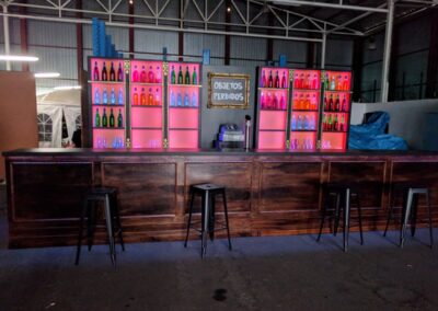 Barra de bar con botelleros iluminados en rosa, montada en el taller