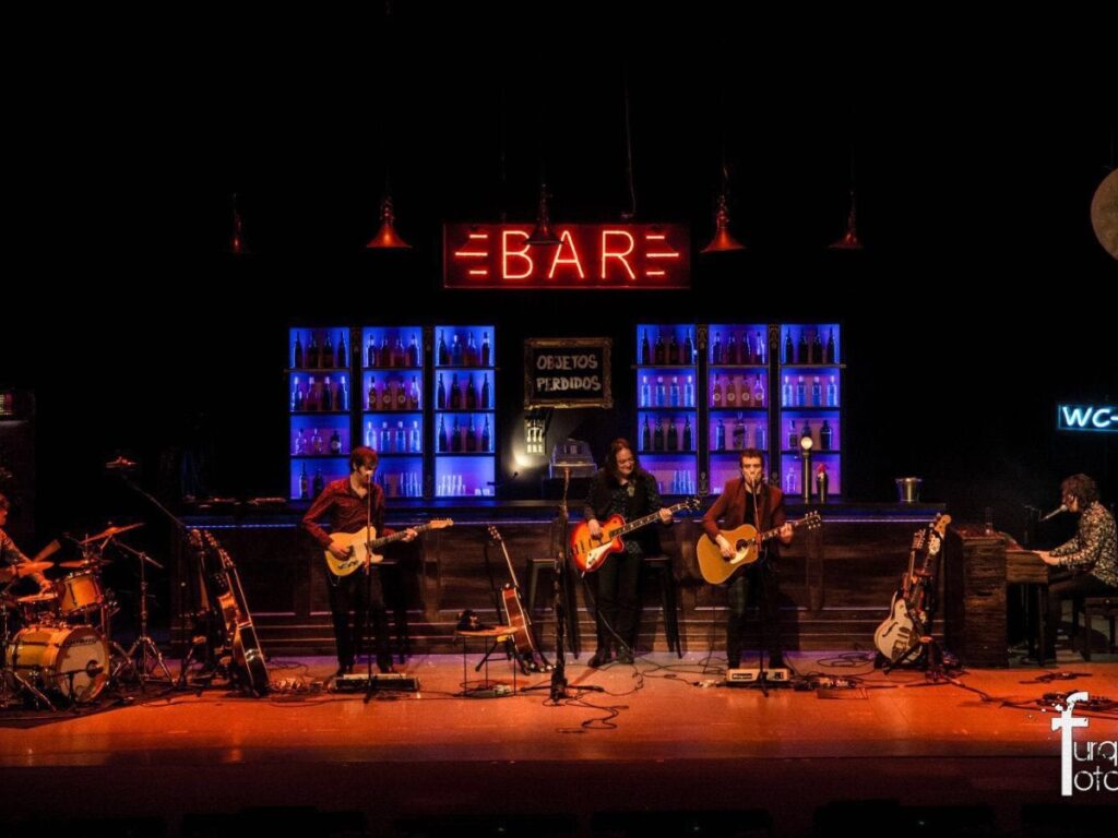 Escenario con barra de bar, botelleros iluminados en azul y un letrero de neón BAR
