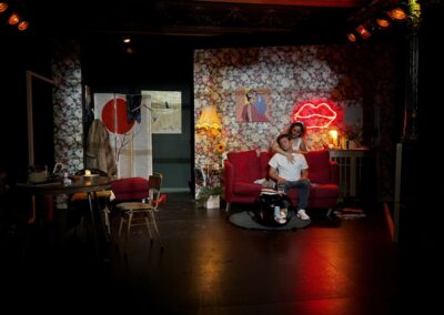Escena de la obra FAN: una pareja en un sofá rojo junto a un neón de unos labios