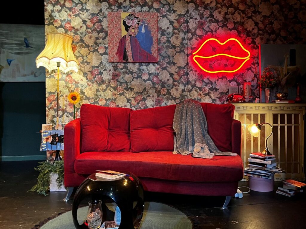 Escenografía de la obra FAN: salón con papel pintado de flores, sofá rojo y neón de unos labios