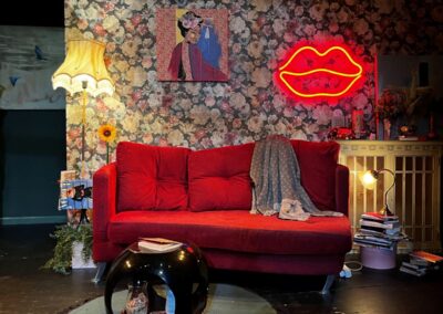 Escenografía de la obra FAN: salón con papel pintado de flores, sofá rojo y neón de unos labios