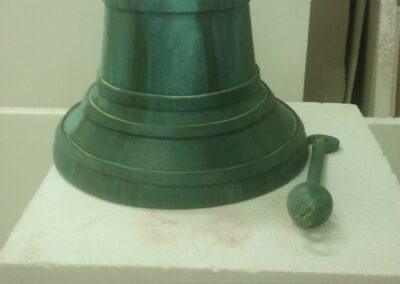 Campana de bronce verde ficticia con su badajo, sobre una peana blanca